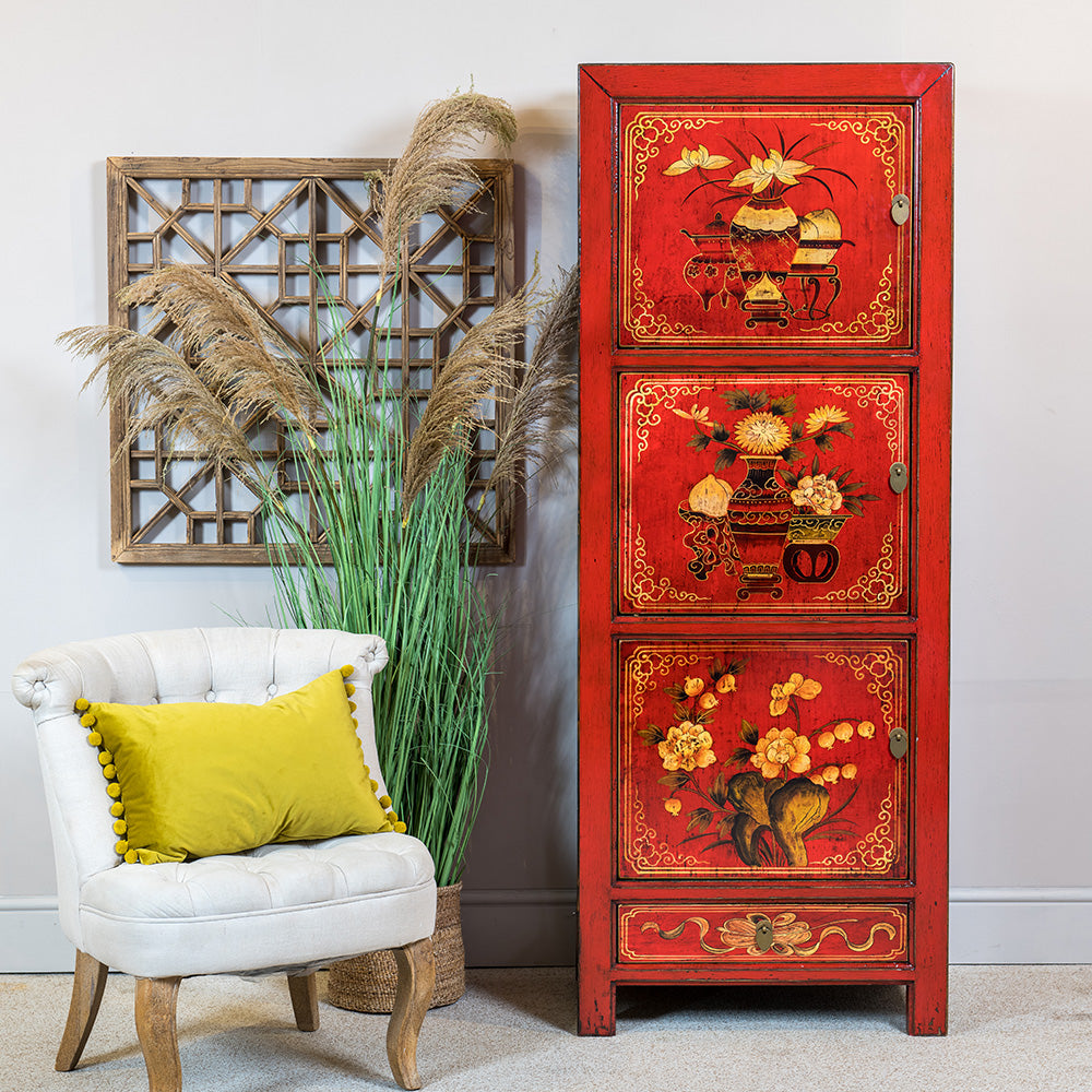 A tall wooden Chinese cabinet with three cupboards and one drawer. The storage unit has a red lacquer finish and the doors are hand-painted in a floral design. 