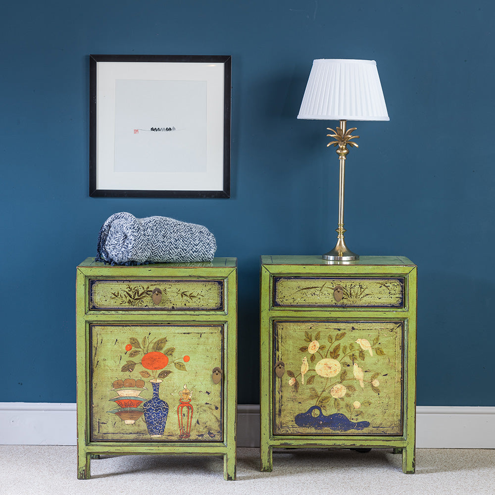 A pair of Oriental wooden green side cabinets decorated with a colourful design. They have a sturdy structure and each have a single drawer. 