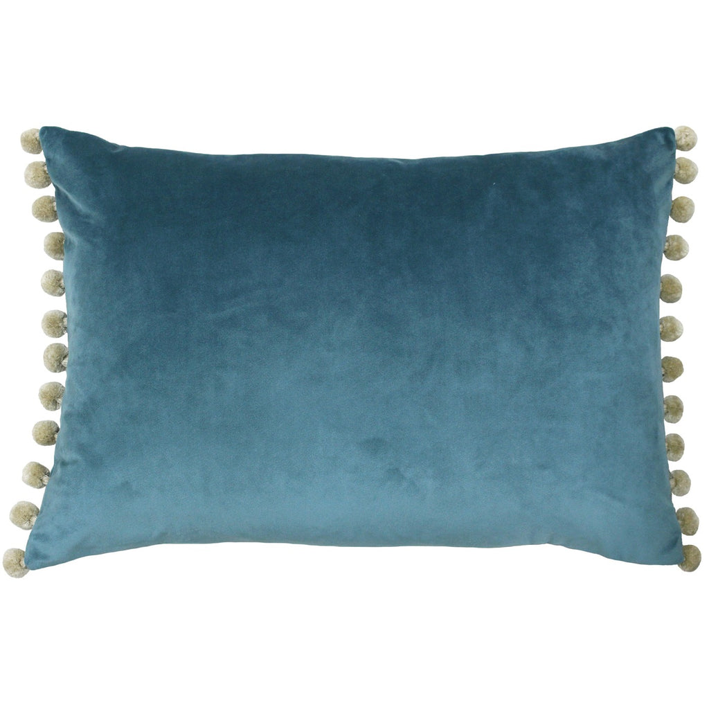 A rectangular cushion with a blue velvet cover with cream pompoms on two of the sides. 