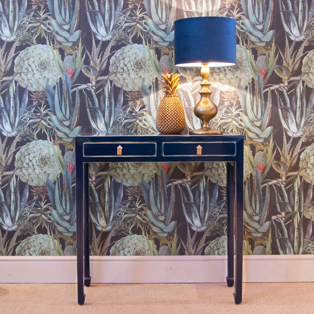 A dark blue lacquered console table with two drawers and brass hardware. 