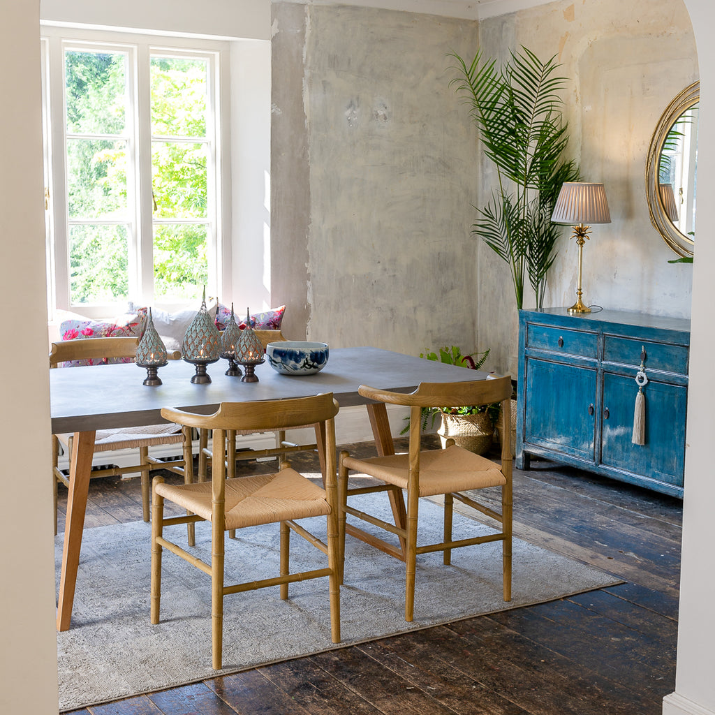 eclectic dining room containing contemporary concrete dining table and natural dining chairs . orchid's blue hampton sideboard brings pop of colour to the dining room. styled with gold mirror and large palm tree