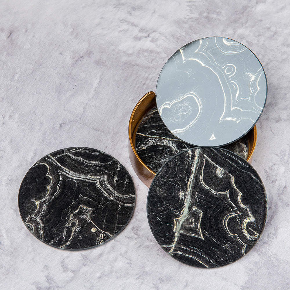 A set of four marble effect black coasters presented in a gold container. 