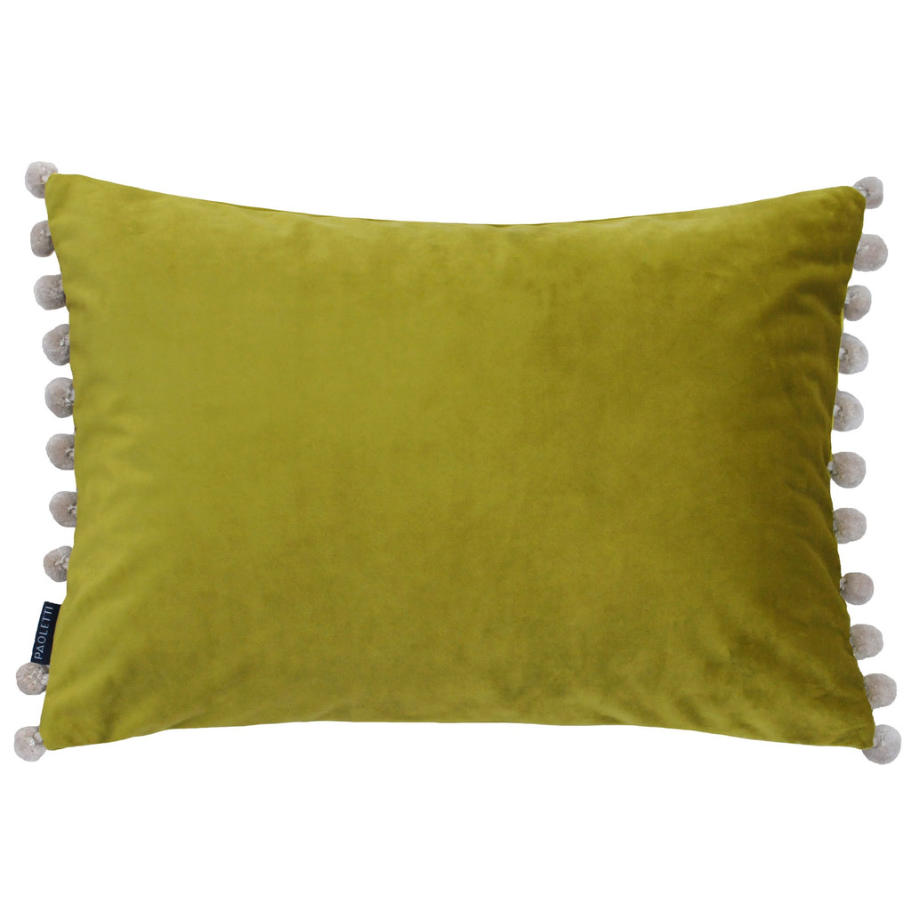 A gold velvet rectangular cushion with cream pompoms down the two shorter edges. 