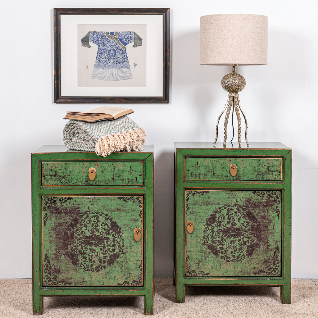 A pair of green wooden cabinets with one drawer, brass handles and floral design.