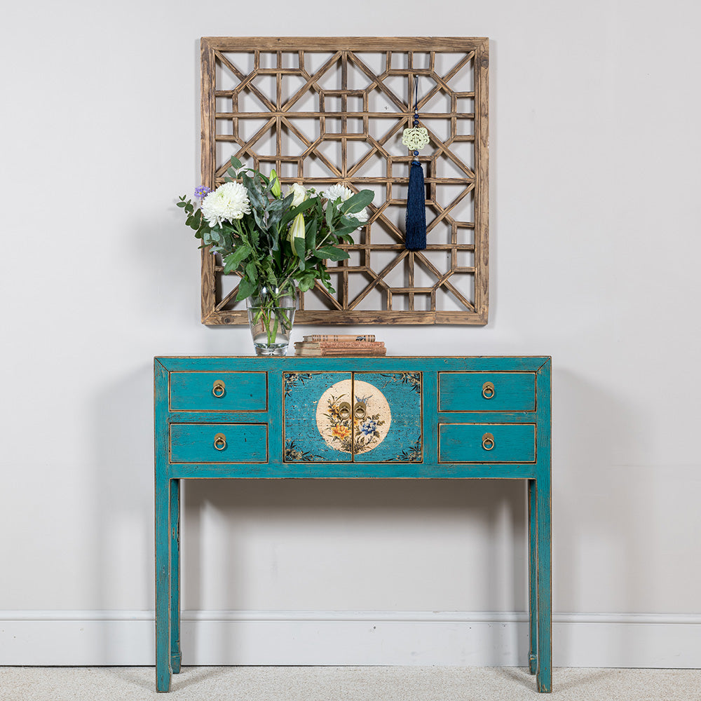 A compact blue console table featuring four drawers and a double cabinet, the doors of which are hand-painted in a floral design. 