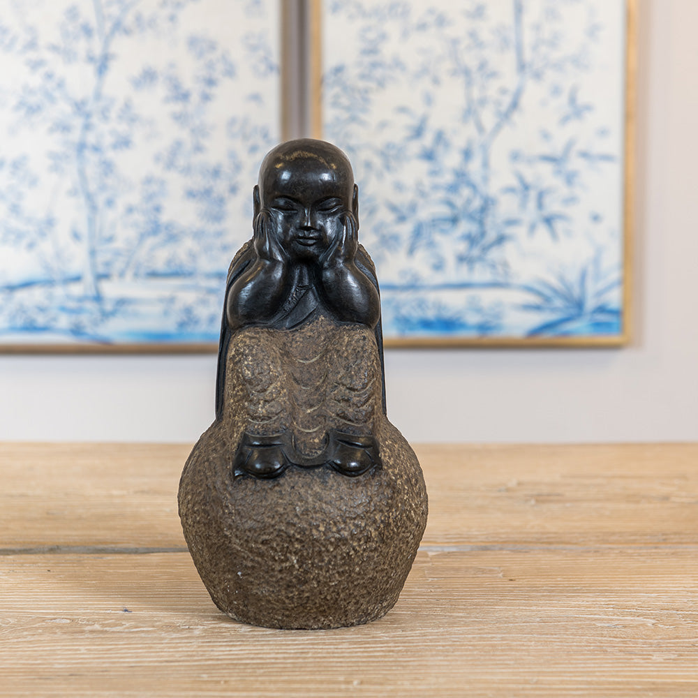 A Chinese Monk sitting with his knees folded up, hands on his cheeks and eyes closed. Handmade out of granite. 