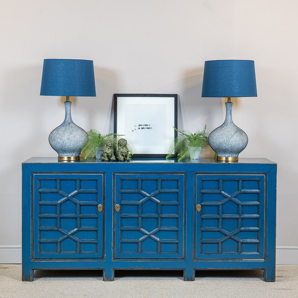 A blue sideboard featuring three cupboards. Each of the doors is hand-curved with a fretwork pattern and has brass hardware. 