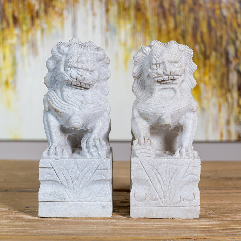 Two hand-carved white stone lions. The male has one of its paws on a ball and the female one has its left paw on a cub. 