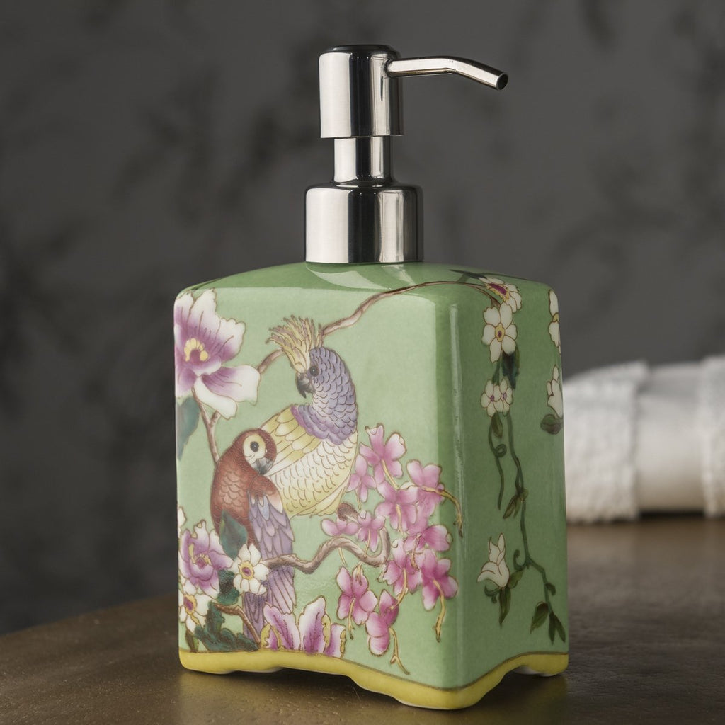 A soap dispenser made of porcelain, hand-painted green and decorated with colourful parrots. 
