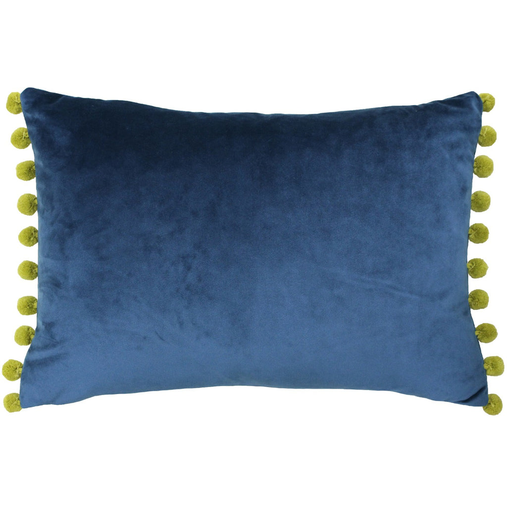 A rectangular cushion with a navy blue velvet cover that has gold pompoms attached to two sides. 