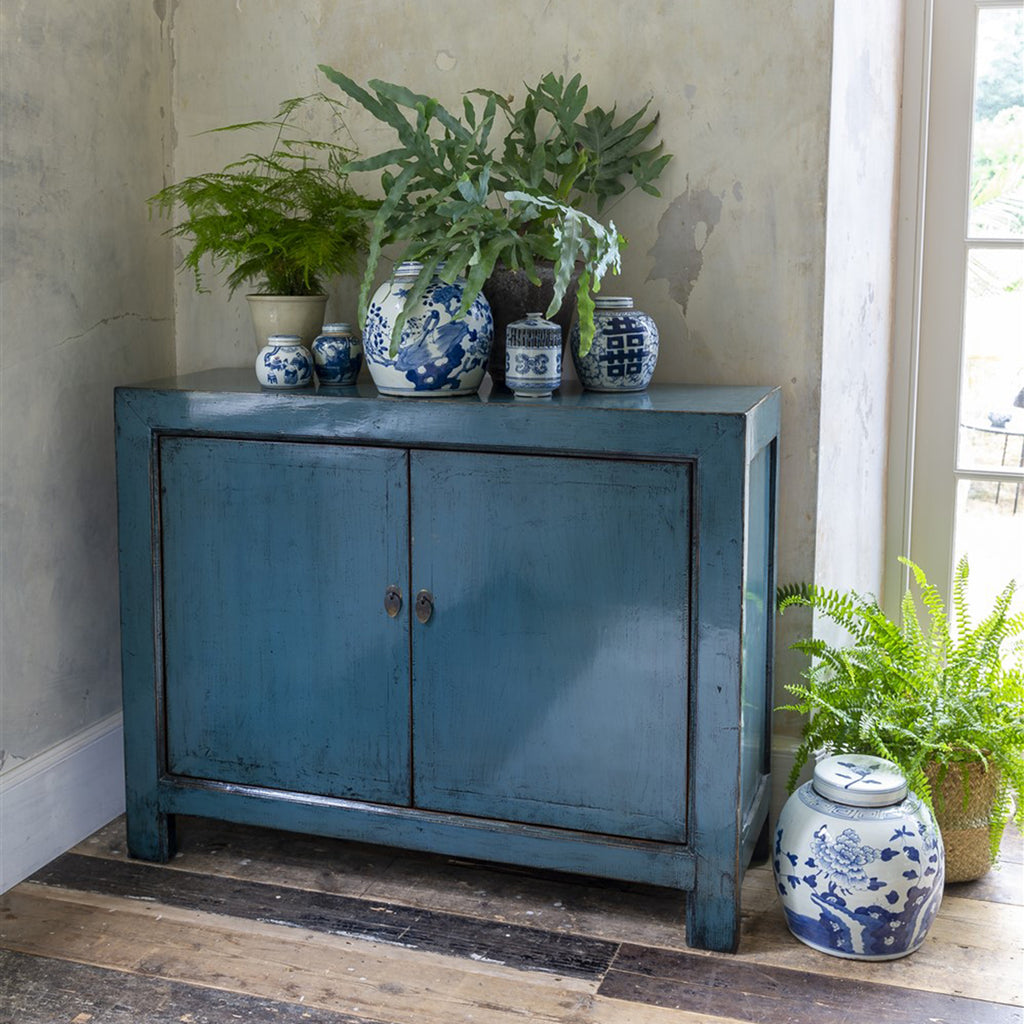 A double door wooden cabinet with brass hardware and hand-finished in blue gloss lacquer.