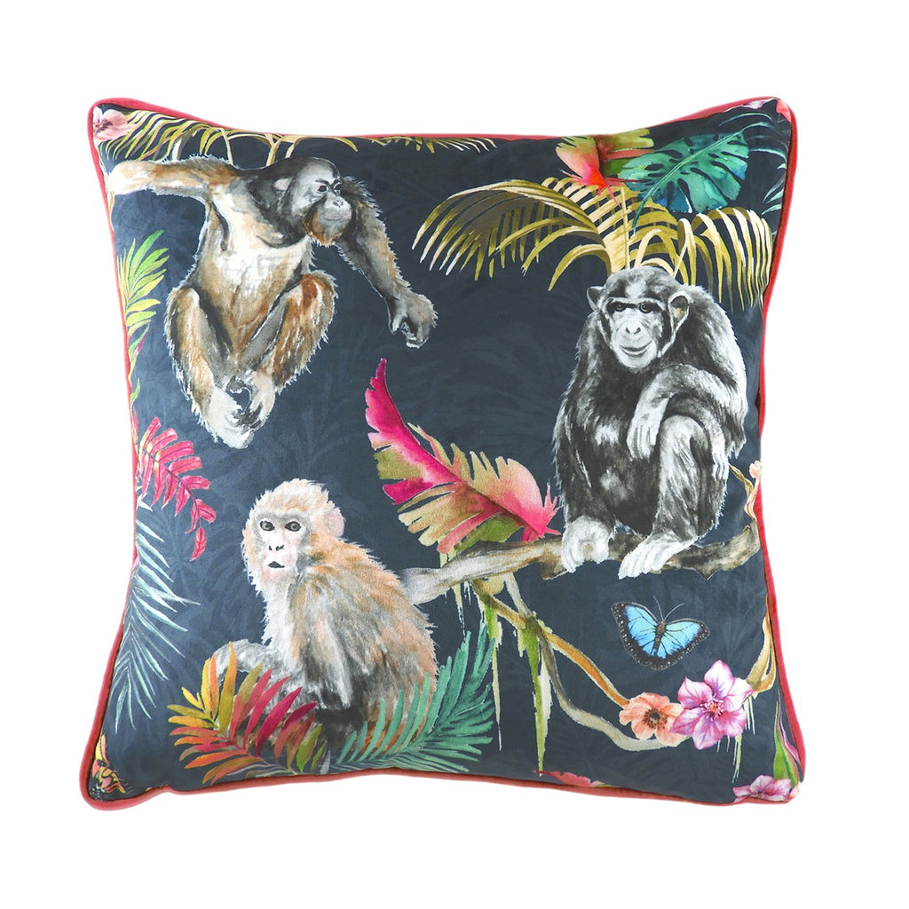 A large square cushion with a velvet dark blue cover, decorated with monkeys and tropical flora and edged with a pink piping. 